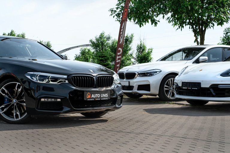 Zwei BMW-Fahrzeuge, ein schwarzer und ein weißer, stehen auf einem gepflasterten Platz.