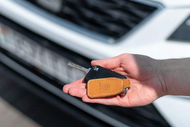 Hand hält einen Autoschlüssel vor einem weißen Fahrzeug.