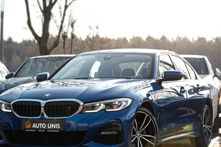 Blauer BMW 3er parkt in einer sonnigen Umgebung zwischen anderen Autos.